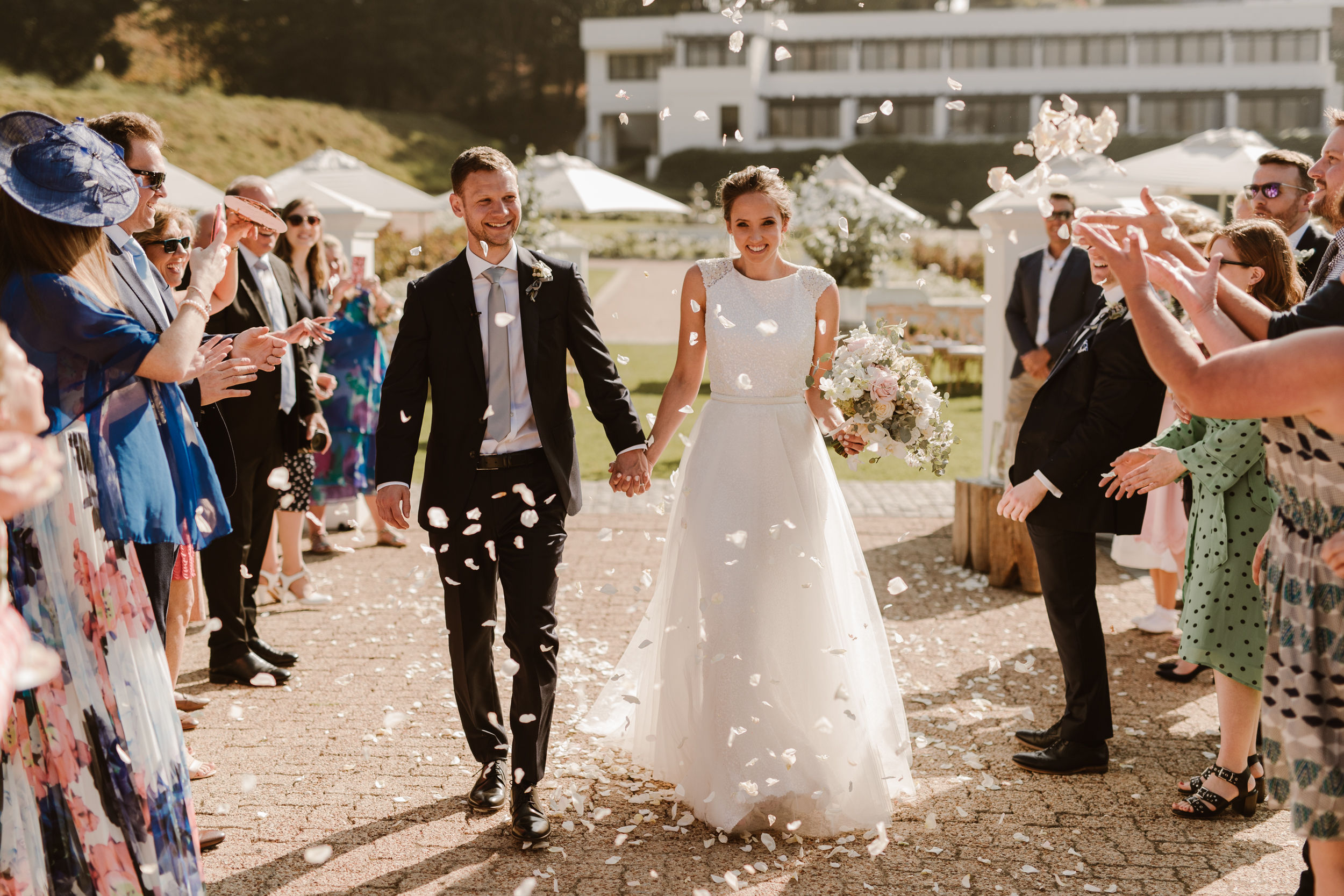 The bride and groom greet the crowd, who throws white rose petals over them after their socially conscious wedding in Cape Town, South Africa.