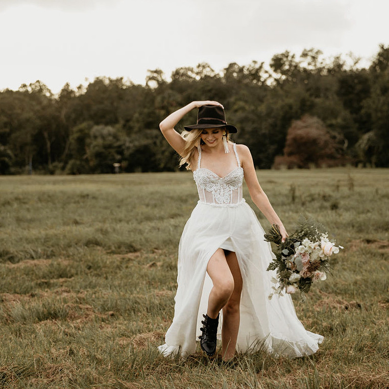 A bride walks through an open green field wearing an ethical wedding dress from vendors Krustallos Couture