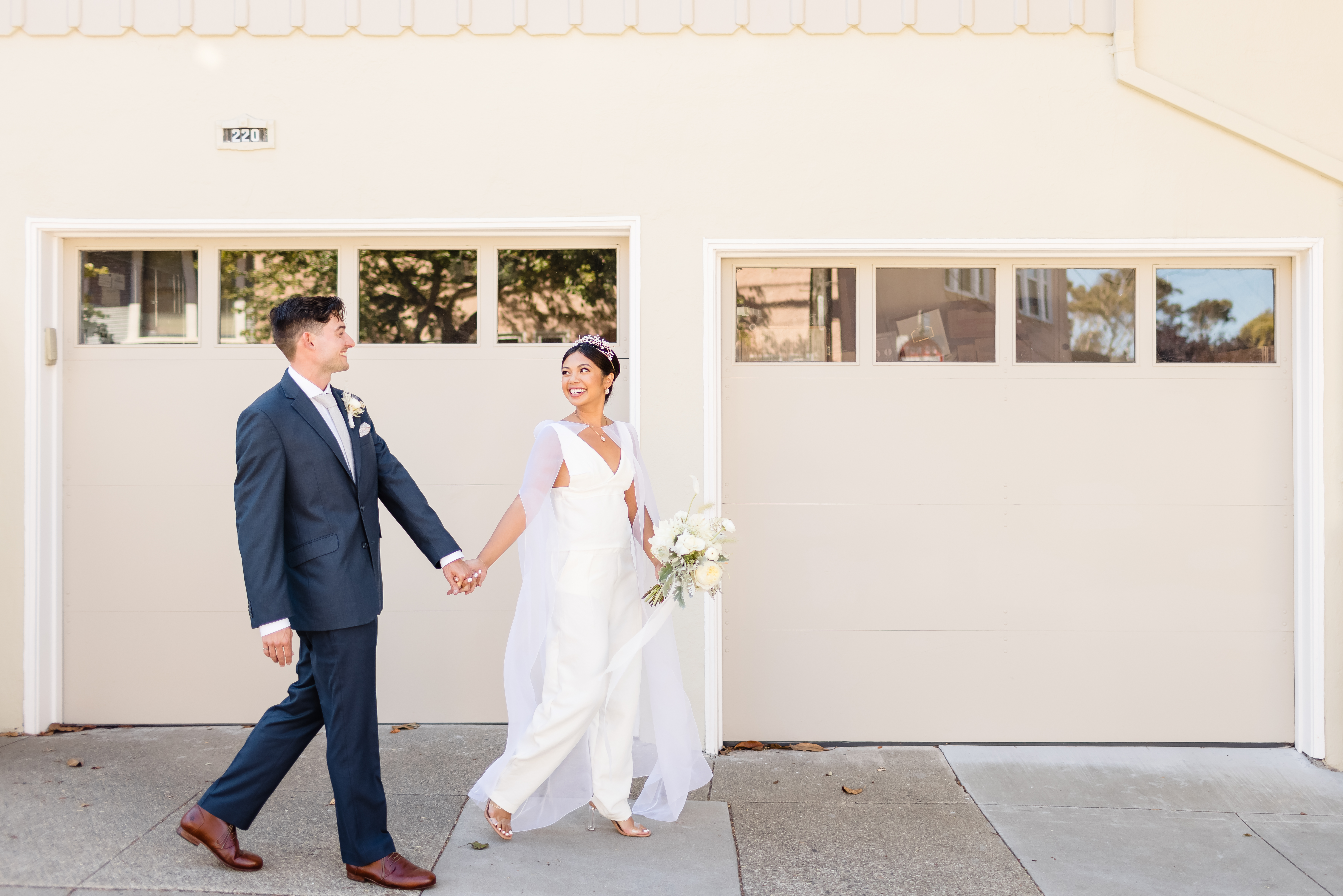 Praise & Barry wedding photo walking in front of tan garage holding hands